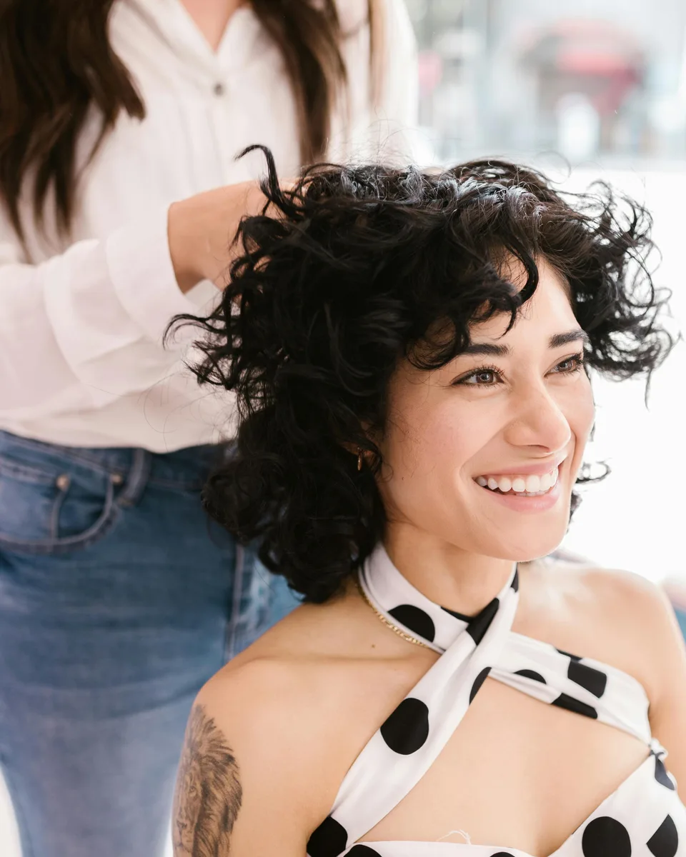 A SalonDemo client smiling after her cut, finished by a stylist behind her